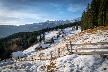 Snow-covered mountain village with wooden houses and fences.
