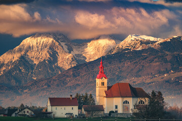 Church with red roof against snowy mountains at sunset.