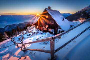 Snowy mountain cabin bathed in golden sunrise light.