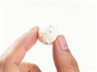 Macro Shot: Fingers Holding a Single Puffed Makhana (Fox Nut) Against a Clean White Background; Healthy Indian Snack Detail