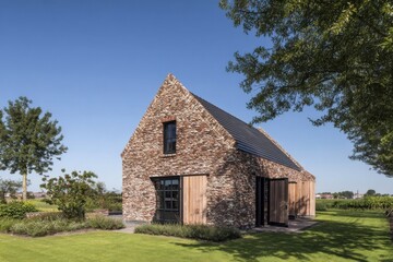 Obraz premium A contemporary brick house featuring beautiful wooden accents is nestled within a vibrant green landscape, all beneath a bright blue sky on a lovely sunny day