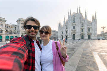 Happy couple taking selfie in front of Duomo cathedral in Milan, Lombardia - Two tourists having...