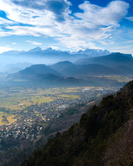 Fototapeta premium Misty mountains overlook a village and valley under blue skies.