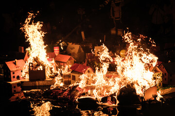 Cardboard houses burn in a fiery display at night.