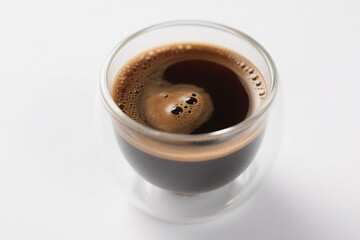 A transparent double-layer glass coffee cup filled with rich dark brown liquid, featuring a dense layer of fine foam on top with tiny bubbles clinging to the inner wall