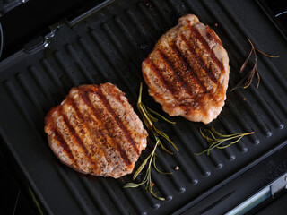 Close-up of marbled beef steaks grilling on an electric grill.