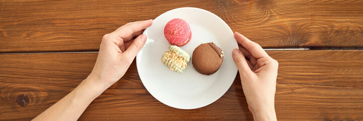 Hands holding plate with colorful macarons on wooden table.