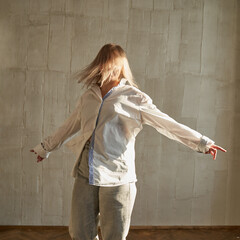 Young caucasian female dancing freely in sunlit room wearing casual outfit.