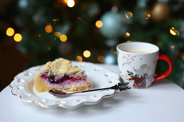 Cozy Christmas scene with cake slice and festive blue mug on table, warm bokeh lights in background