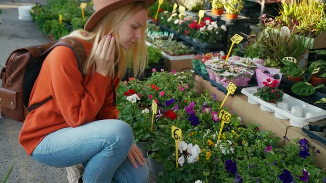 Beautiful blonde woman wear hat and smelling fresh bouquet of yellow sunflowers while shopping at an outdoor flower market stall, enjoy fragrant scent of blooms