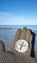 Compass in a hand with a sea in the background, selective focus