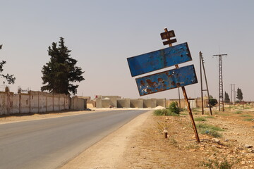 War-damaged old road sign reading Aleppo at the entrance of the Syrian city, full of bullet holes and rust. Reflects the impact of the Syrian Civil War, symbolizing destruction, and resilience. Syria © Dr.MYM