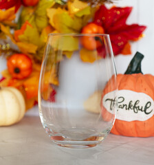 Clear glass on light background with pumpkins and leaves. Transparent drinkware mockup for product presentation or branding design.