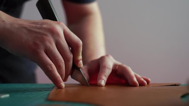 Cutting leather with knife and ruler 4k video. The artisan uses a knife and ruler to shape pieces of genuine leather for handmade goods. Artisans trim edges and prepare genuine leather.
