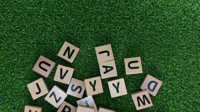 Wooden alphabet tiles scattered across a vibrant green surface