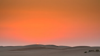 Obraz premium Dramatic desert sunset with orange sky and sand dunes creates a serene and vast landscape