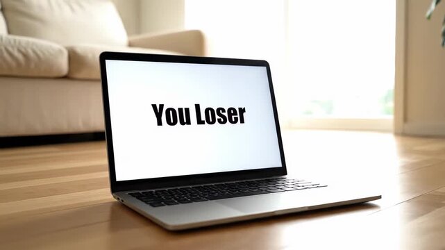 The laptop screen displays an offensive message that reads You Loser, with the computer positioned on the floor to represent the prevalence of online hate and bullying