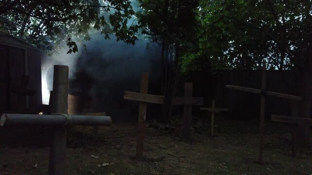 A zombie walking through a rustic cemetery graveyard with crosses and smoke. Classic suspense horror or Halloween film theme. 