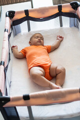 Baby sleeping peacefully in crib wearing orange onesie