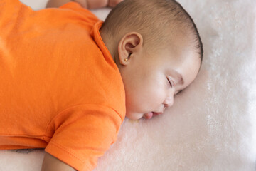 Baby sleeping peacefully on white blanket wearing orange onesie
