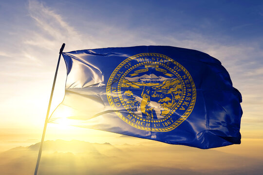 Nebraska state of United States flag textile cloth fabric waving on the top sunrise mist fog