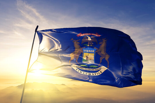 Michigan state of United States flag textile cloth fabric waving on the top sunrise mist fog