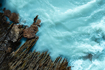 A rushing turquoise river is striking against the dark, layered rock.