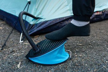 Person inflates the air mattress with a foot pump near a tent in the woods.