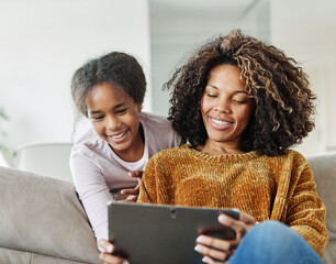 Teenage girl sitting at sofa with her mother and using tablet computer. Mother and daughter bonding and having fun at home