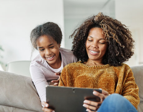 Teenage girl sitting at sofa with her mother and using tablet computer. Mother and daughter bonding and having fun at home