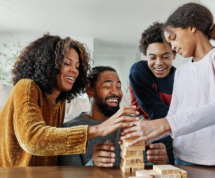 Portrait of a happy african american family at home, having fun playing wooden brick challenge game, playing board game jenga at home - Powered by Adobe
