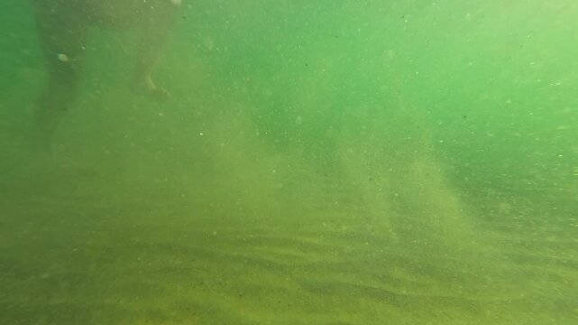 Under water Young girl walking in slow motion through lake sunny day sandy bottom