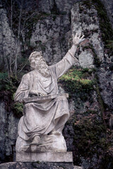 Obraz premium Ancient Stone Statue of Prophet or Sage with Raised Arm Against Rocky Cliff