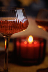 Close detail of coupe glass with bubbly rose wine next to candle in cozy seasonal setting