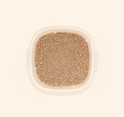 Brown cat litter granules in a transparent container against a soft pastel background that highlights their texture and color, perfectly suited to the concept of pet care