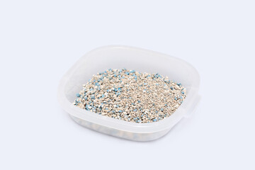 Transparent container holds textured granules of cat litter with blue flecks highlight the natural absorbent materials on a white background, suitable for pet care.