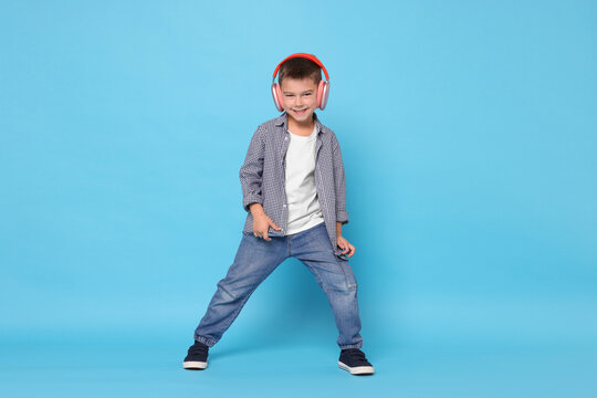 Little boy with wireless headphones dancing on light blue background