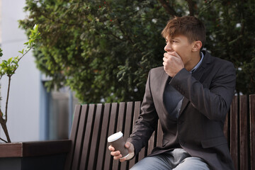 Obraz premium Young man with cup of drink suffering from nausea outdoors, space for text