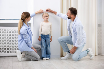Parents marking their daughter's height on white wall at home