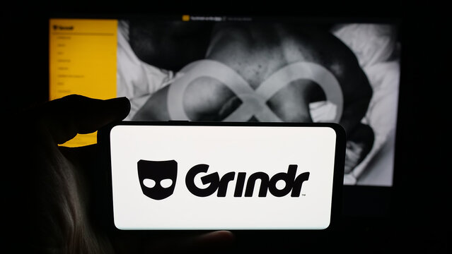Stuttgart, Germany - 10-15-2025: Person holding cellphone with logo of LGBT social media platform company Grindr Inc on screen in front of webpage. Focus on phone display.
