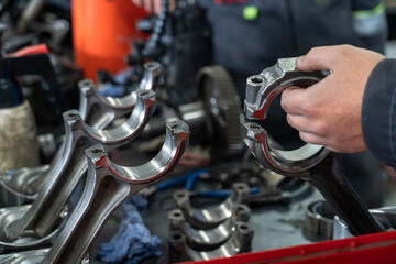 Mechanic holding shiny connecting rod at engine repair workshop, showcasing precision engineering,...