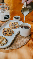 A person is pouring milk into a cup next to a tray of cookies