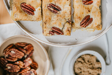 A plate of three peanut butter bars sits on a table next to a bowl of peanuts