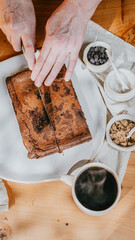 A person is cutting a chocolate cake with a knife on a white plate