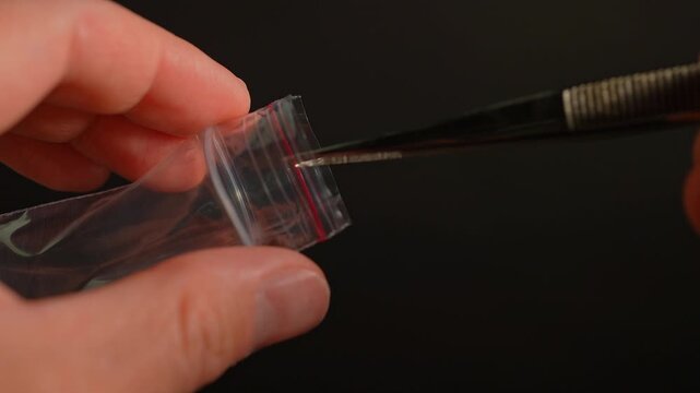 Hands of the drug dealer show off LSD strip blotter in small plastic bag. Dry drops of Lysergic acid drug on paper tabs lucy for sale in club, party and street. Illegal drugs trafficking.