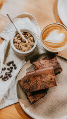 A plate of brownies sits on a table next to a cup of coffee