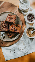 A plate of brownies sits on a wooden board with a white cloth underneath