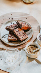 A plate of brownies sits on a wooden board with a bowl of coconut flakes