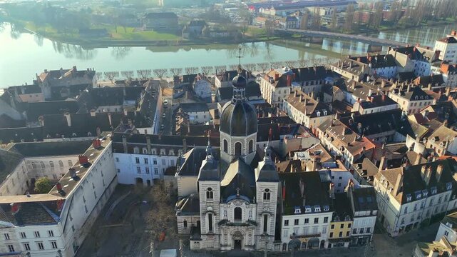 Drone footage capturing baroque church surrounded by terracotta roofs with waterway visible behind under crisp morning sunlight 