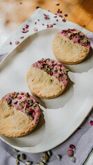 Three cookies with pink frosting and green sprinkles on a white plate